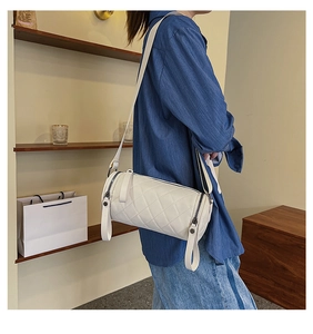 Close-up of white quilted cylinder crossbody bag with adjustable strap and metal zipper