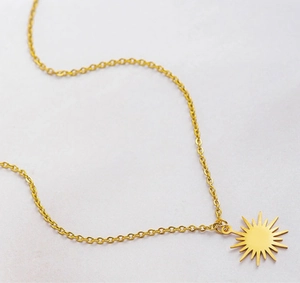 Detailed view of an 18K gold plated stainless steel sun pendant necklace on grey texture