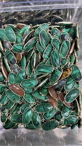 Macro shot of bulk turquoise oval stone connectors with gold plated edges in a container