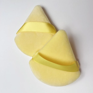 Close-up of two yellow triangular velvet makeup puffs with satin ribbon handles