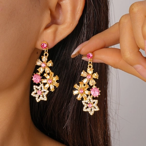 Macro view of gold flower earrings with pink rhinestones and tassels worn by a model