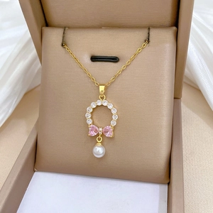 Detailed view of gold necklace with pink zircon bow and white pearl pendant