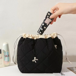 Placing hand cream into black quilted makeup bag with drawstring and bow detail