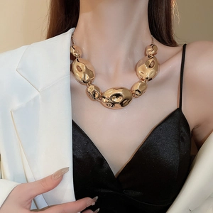 Close-up of chunky gold-toned statement necklace featuring oversized irregular metallic beads