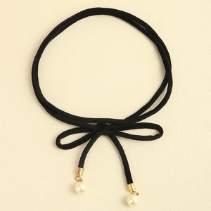Detail of a black velvet choker with a bow and gold-capped pearls on a cream background