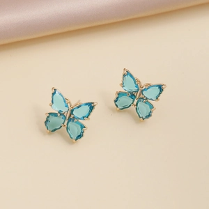 Close-up of blue crystal butterfly earrings on elegant beige silk fabric background