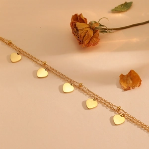 Double-layer gold stainless steel bracelet with five heart charms on a warm sand background