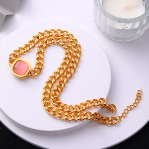 Gros plan d'un collier chaîne gourmette dorée avec un pendentif carré rose translucide
