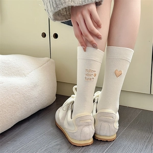 Detail of beige cotton socks with heart embroidery worn with white sneakers