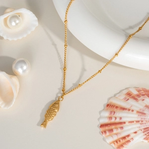 Detail of fish pendant on a fine gold chain with beach-themed decor and pearls