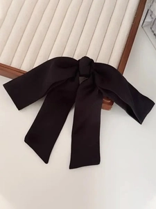 Detail of the black satin oversized bow hair clip on a neutral background