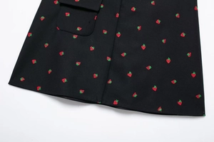 Gros plan de la broderie fraise sur tissu noir avec détail de poche à rabat