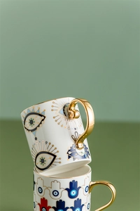 Detail of stacked ceramic mugs with Evil Eye and Hamsa Hand motifs and gold handles