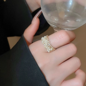 Close-up of gold-plated pearl and cubic zirconia ring on finger holding a glass