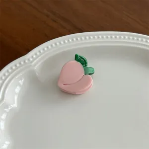 Detailed view of a sweet pink peach-shaped hair clip on a white ceramic tray decoration
