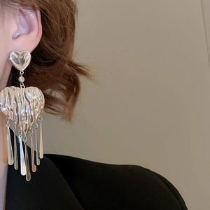 Macro shot of silver heart tassel earrings with crinkled metal texture on a model