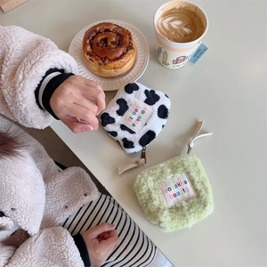 Plush mini makeup bag with cow print and light green fabric on a soft cafe tabletop