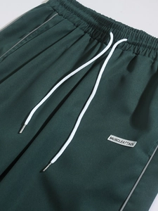 Detail of dark green jogger pants with white drawstring and muscleattack woven label