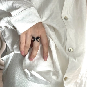 Detail of beaded black bow ring on finger with white linen shirt background