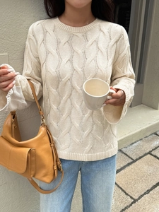 Detail of off-white knit sweater showing thick cable stitch texture and cozy round neck