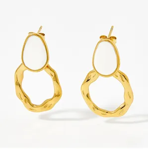 Close-up of gold-plated hoop earrings with white enamel inserts and wavy texture
