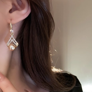Close-up of vintage gold triangle earrings with crystals and pearl pendant on model