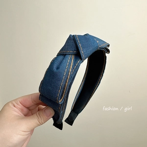 Detail of blue denim wide headband with orange contrast stitching and top knot design