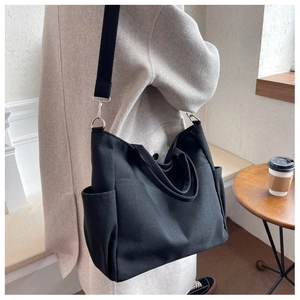 Detail of a black canvas tote bag showing functional side pockets and wide strap