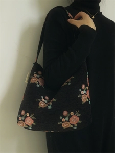 Detail of vintage floral embroidery on black canvas shoulder bag with small brand label