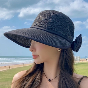 Women's black woven straw sun hat with large brim and bow detail on beach background