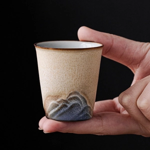 Vue à la main d'une tasse à thé en céramique avec glaçure beige mate et reliefs montagneux