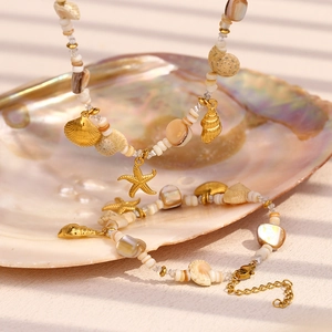 Macro detail of 18K gold starfish and seashell charms on a white bead necklace