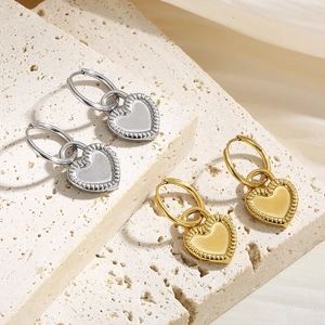 Gold and silver heart drop earrings with textured borders on minimalist stone background