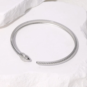 Minimalist silver snake-shaped open bracelet with detailed scales on white rock background