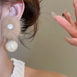 Detail shot of khaki fur ball earrings with zircon studs and white pearls on a model