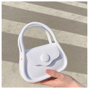 Mini white macaron jelly bag with silver chain held over an outdoor urban street background