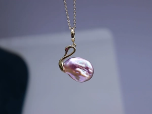 Gros plan du pendentif cygne doré avec une perle baroque violette et une pierre rouge