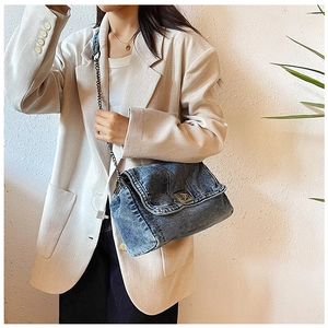 Detail of blue denim crossbody bag with metal twist lock and chain strap on model
