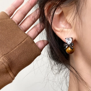 Close-up of heart-shaped zircon earrings with black bow and tiger eye stone beads