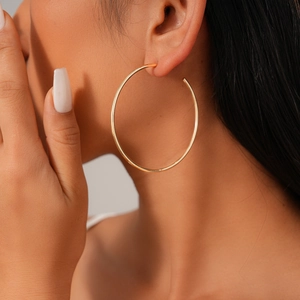 Minimalist large golden geometric circle hoop earrings worn by a model in a close-up view