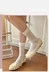 Detail von Mesh-Ballerina-Socken mit Lederschleife und geblümten flachen Schuhen zu Hause