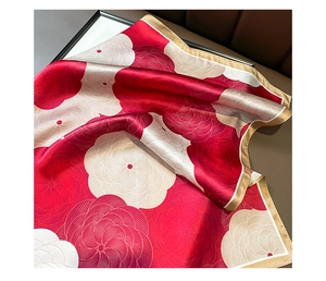 Macro detail of a red and white floral silk square scarf with golden borders on leather