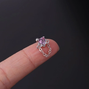 Detailed macro shot of a pink heart zircon stud earring with a silver chain held by hand