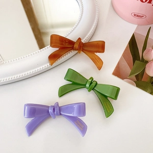 Close-up of handmade acetate bow hair clips in amber, green and purple colors