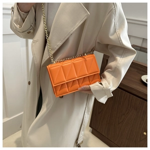Detail shot of bright orange quilted leather bag with elegant gold chain strap and stitching