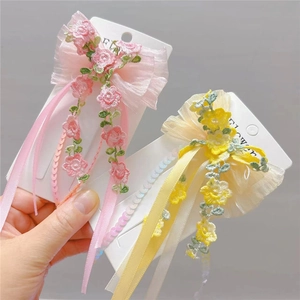 Detail of floral embroidery and sequin tassels on pink and yellow ribbon hair clips