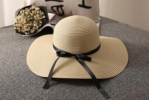 Close-up of woven beige straw hat with black silk bow ribbon on a textured surface
