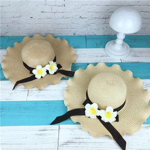 Detail of wide-brimmed straw sun hats featuring plumeria flowers and black grosgrain ribbon