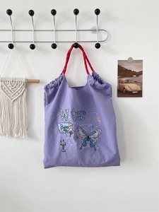 Close-up of purple embroidered tote bag with red braided handles and butterfly print