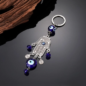 Macro detail of Hamsa hand keychain with blue evil eye beads on reflective black surface